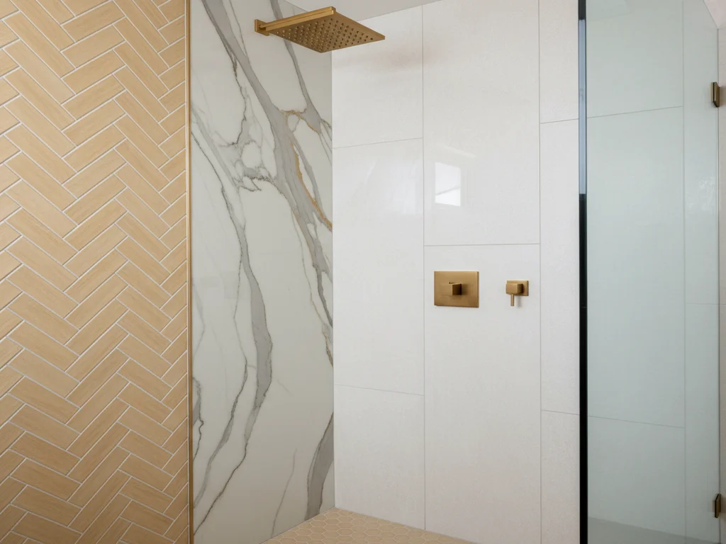 Sacramento bathroom tile installation featuring large-format 24x48 porcelain shower walls, herringbone niche detail, brushed-gold rainfall fixtures, and full Schluter Kerdi waterproofing membrane.